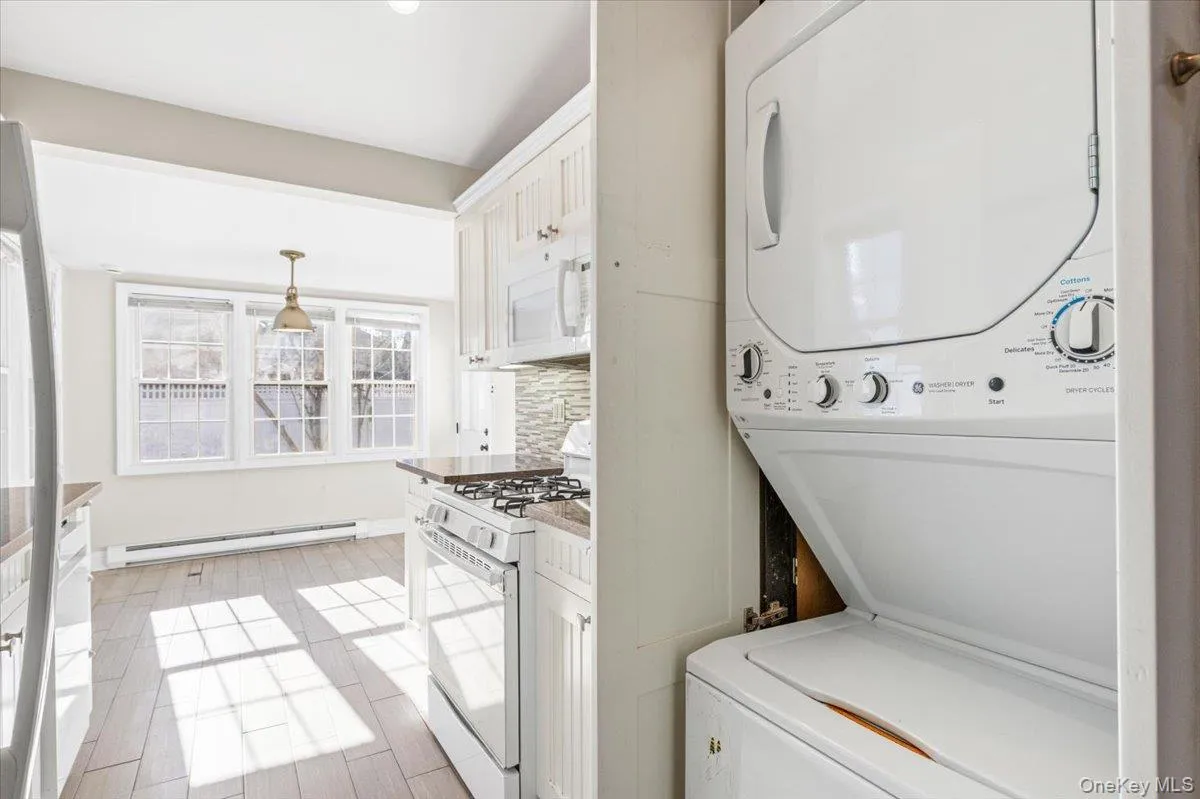 Laundry room with baseboard heating, stacked washer / drying machine, and light wood-style floors Laundry room with baseboard heating, stacked washer / drying machine, and light wood-style floors