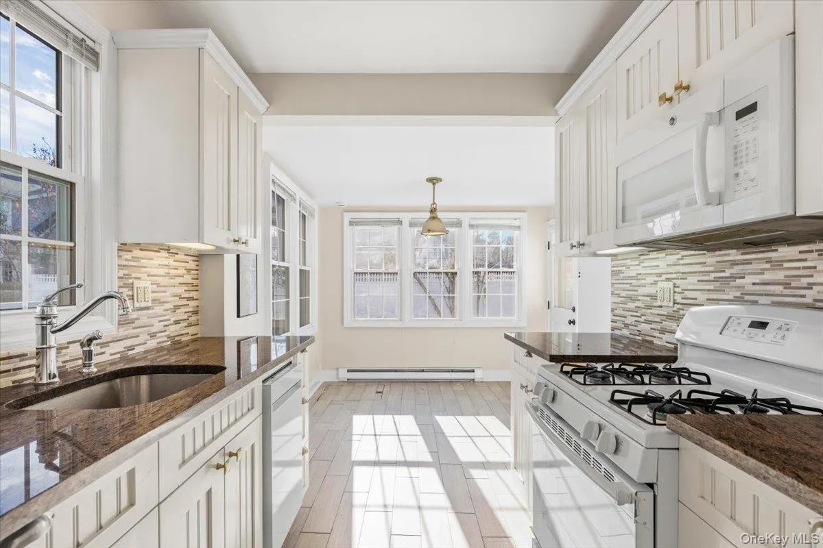 Kitchen featuring white appliances, tasteful backsplash, dark stone countertops, and plenty of natural light Kitchen featuring white appliances, tasteful backsplash, dark stone countertops, and plenty of natural light
