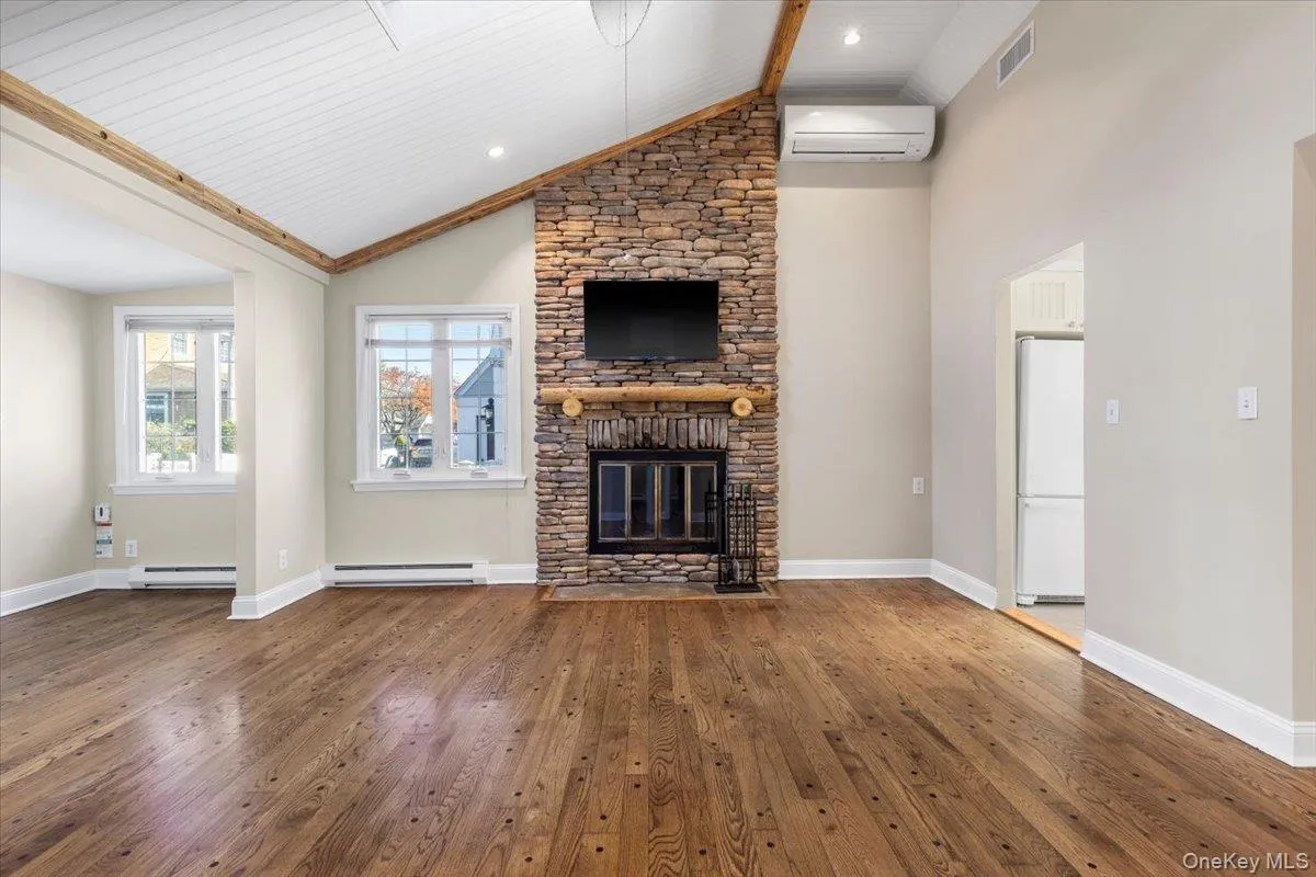 Unfurnished living room with hardwood / wood-style floors, a wall mounted air conditioner, high vaulted ceiling, a fireplace, and a baseboard heating unit Unfurnished living room with hardwood / wood-style floors, a wall mounted air conditioner, high vaulted ceiling, a fireplace, and a baseboard heating unit
