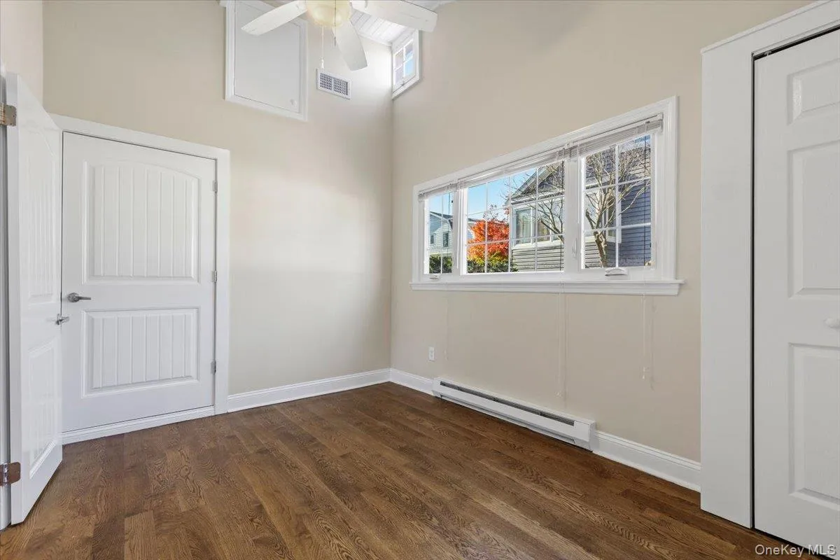 Spare room featuring a baseboard radiator, dark wood-style flooring, a ceiling fan, and a towering ceiling Spare room featuring a baseboard radiator, dark wood-style flooring, a ceiling fan, and a towering ceiling