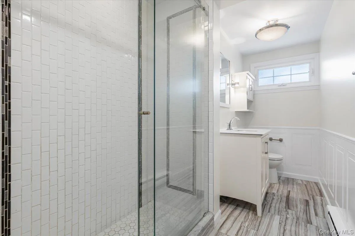 Full bath featuring wainscoting, vanity, a stall shower, a baseboard radiator, and a decorative wall Full bath featuring wainscoting, vanity, a stall shower, a baseboard radiator, and a decorative wall
