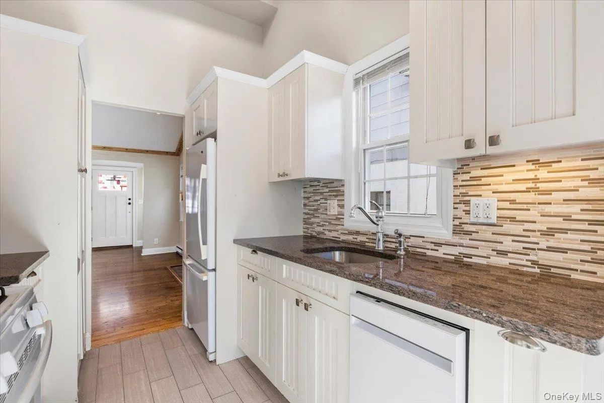 Kitchen with white appliances, dark stone countertops, light wood finished floors, backsplash, and white cabinets Kitchen with white appliances, dark stone countertops, light wood finished floors, backsplash, and white cabinets