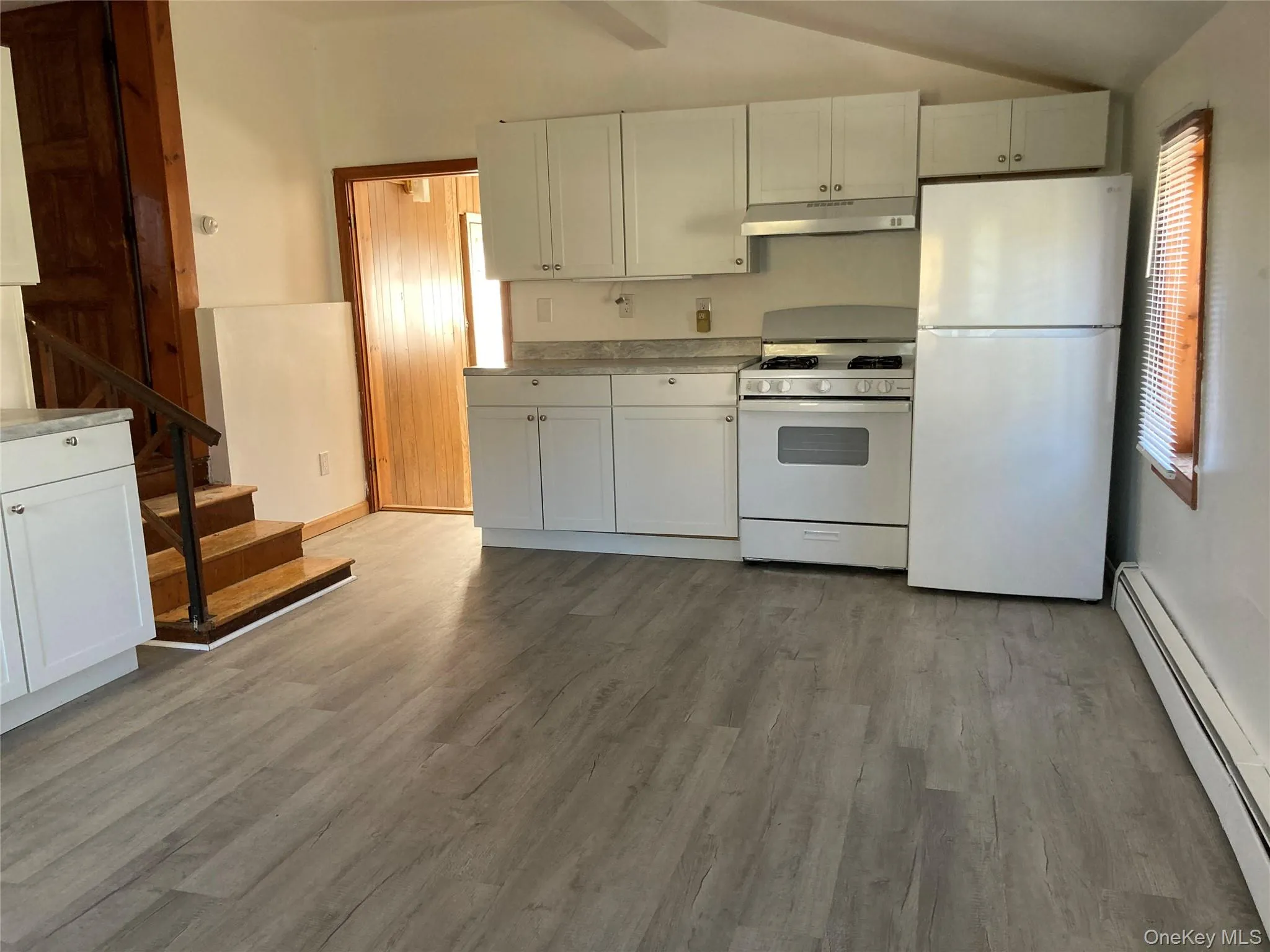 Kitchen featuring baseboard heating, white appliances, white cabinetry, light countertops, and light wood-style flooring Kitchen featuring baseboard heating, white appliances, white cabinetry, light countertops, and light wood-style flooring