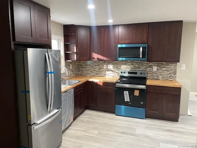 Kitchen with appliances with stainless steel finishes, dark brown cabinetry, backsplash, light wood-type flooring, and open shelves Kitchen with appliances with stainless steel finishes, dark brown cabinetry, backsplash, light wood-type flooring, and open shelves
