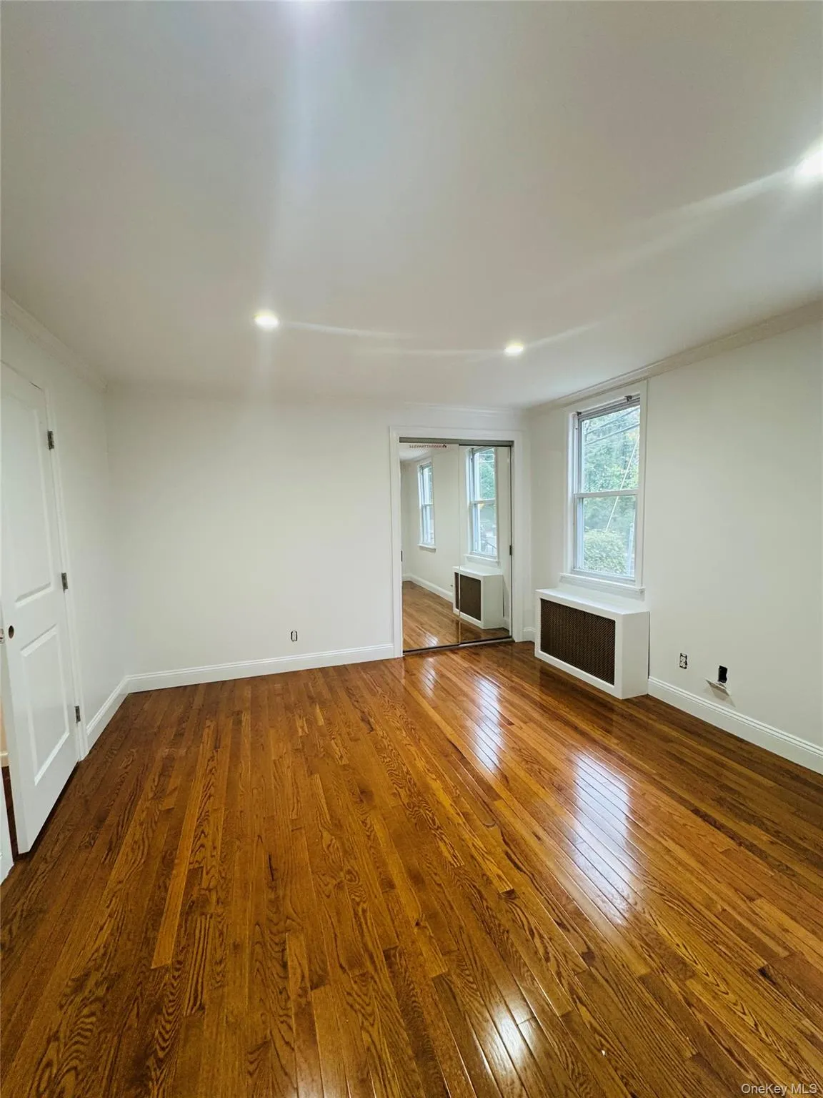 Empty room with ornamental molding, dark wood-type flooring, radiator, and recessed lighting Empty room with ornamental molding, dark wood-type flooring, radiator, and recessed lighting
