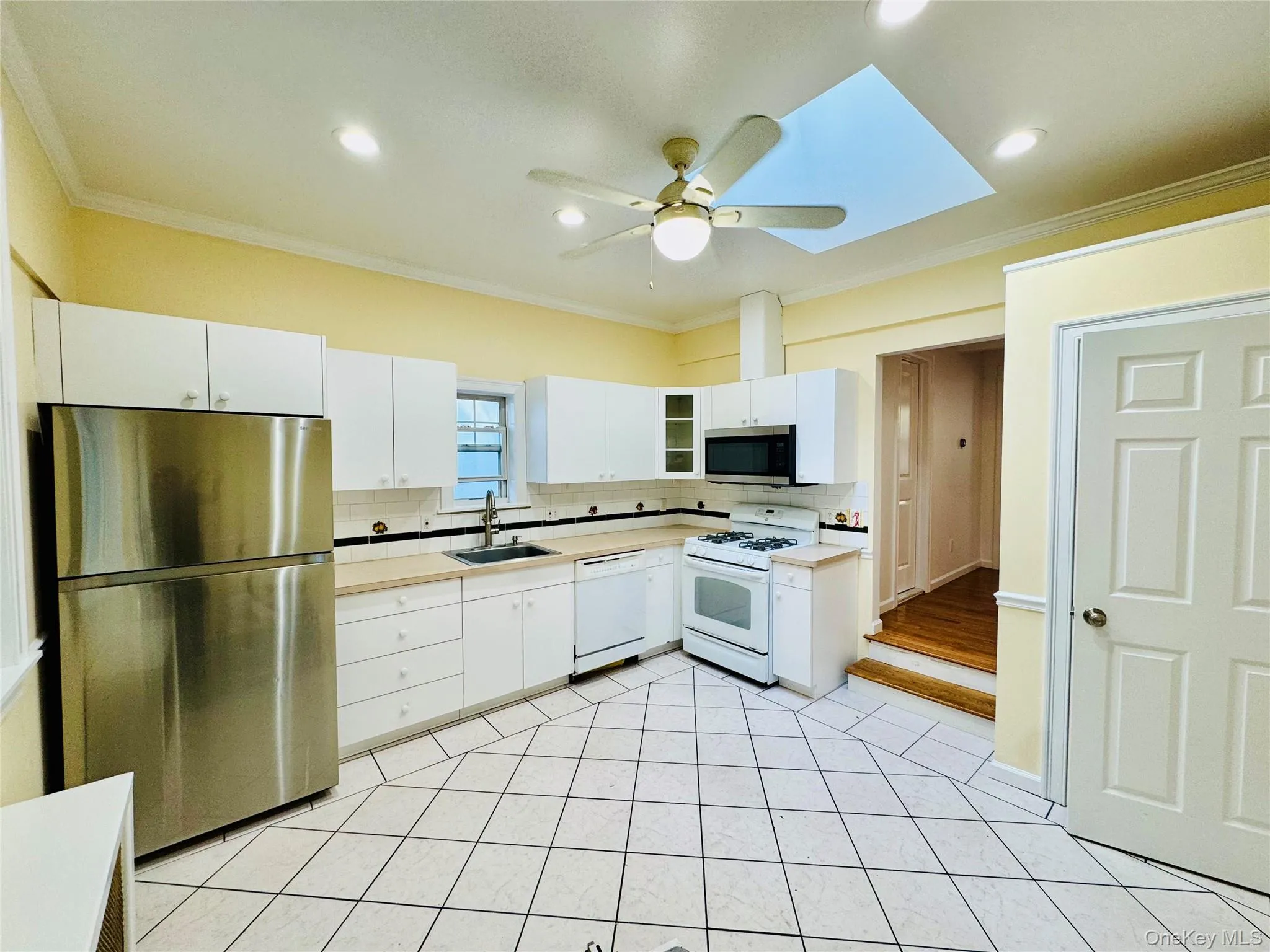 Kitchen with crown molding, stainless steel appliances, light countertops, backsplash, and white cabinetry Kitchen with crown molding, stainless steel appliances, light countertops, backsplash, and white cabinetry