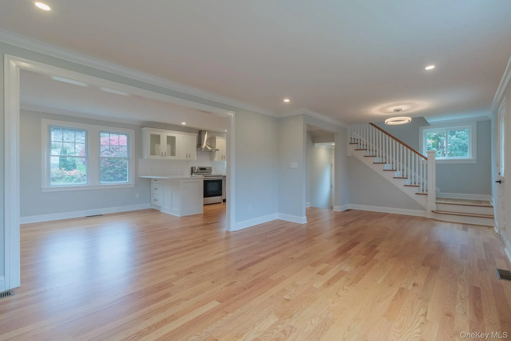 Unfurnished living room with crown molding, stairway, light wood finished floors, and recessed lighting Unfurnished living room with crown molding, stairway, light wood finished floors, and recessed lighting