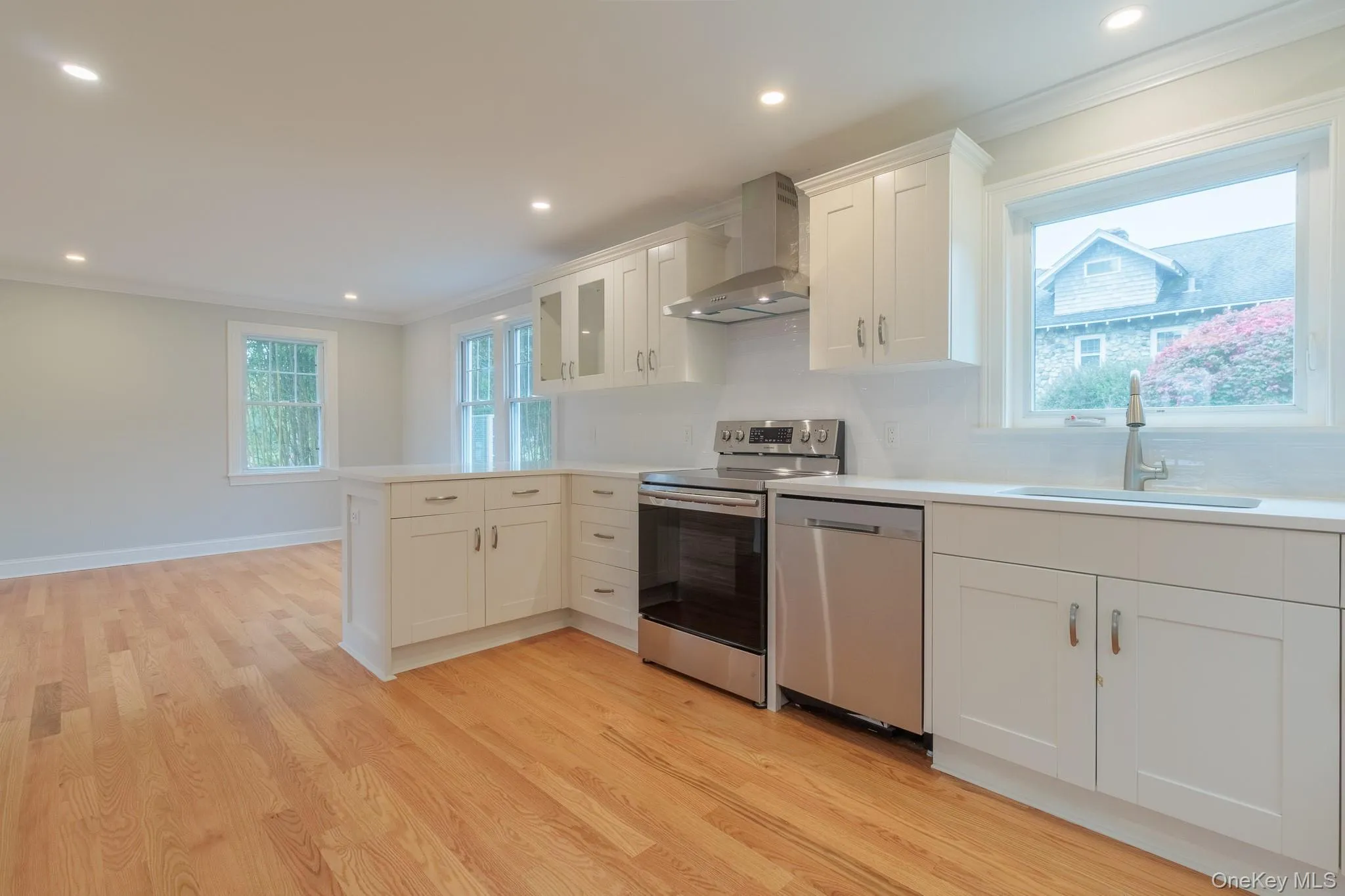 Kitchen with ornamental molding, stainless steel appliances, wall chimney exhaust hood, glass insert cabinets, and white cabinetry Kitchen with ornamental molding, stainless steel appliances, wall chimney exhaust hood, glass insert cabinets, and white cabinetry