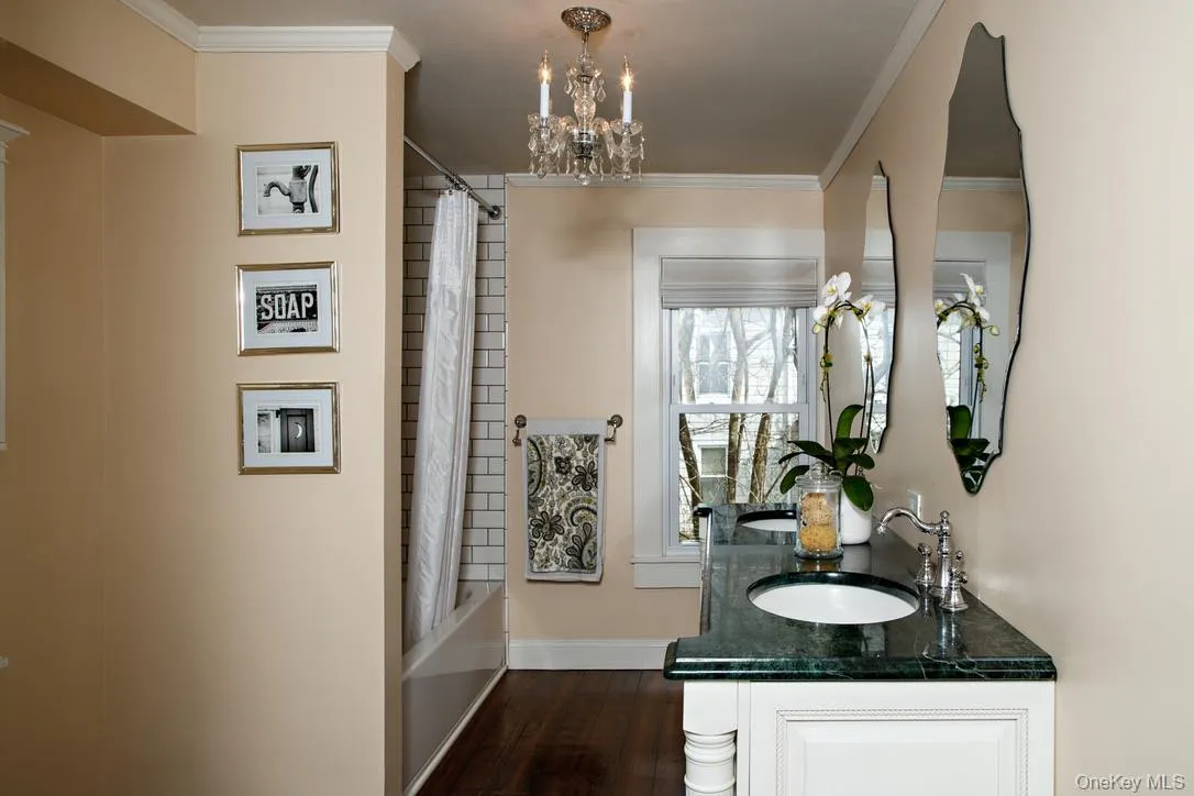 Bathroom with shower / bath combo, crown molding, a chandelier, double vanity, and dark wood-type flooring Bathroom with shower / bath combo, crown molding, a chandelier, double vanity, and dark wood-type flooring