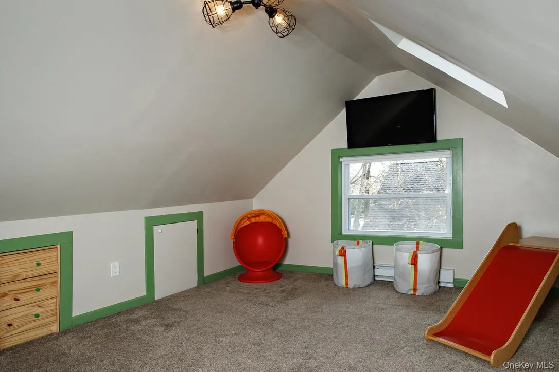 Rec room featuring vaulted ceiling, carpet flooring, a skylight, and baseboard heating Rec room featuring vaulted ceiling, carpet flooring, a skylight, and baseboard heating