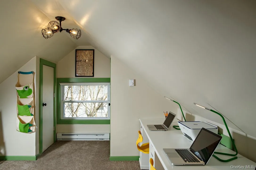 Home office with a baseboard radiator, dark carpet, and lofted ceiling Home office with a baseboard radiator, dark carpet, and lofted ceiling