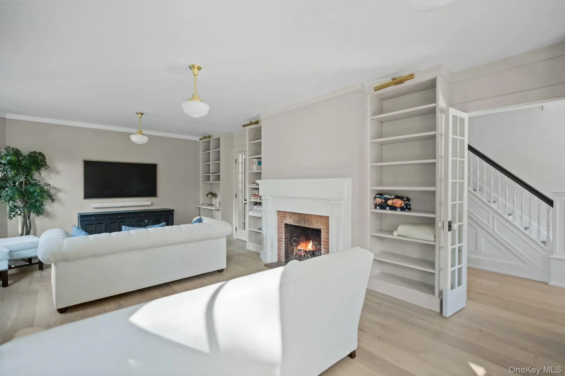 Living room featuring a lit fireplace, stairs, light wood-style floors, and ornamental molding Living room featuring a lit fireplace, stairs, light wood-style floors, and ornamental molding