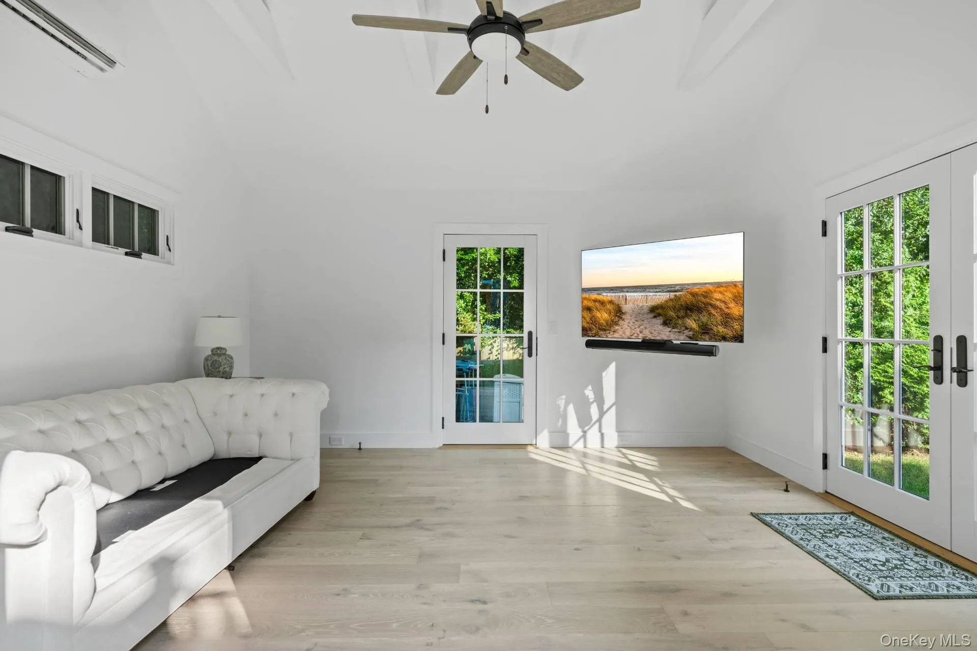 Sitting room featuring light wood-style floors, ceiling fan, vaulted ceiling, french doors, and an AC wall unit Sitting room featuring light wood-style floors, ceiling fan, vaulted ceiling, french doors, and an AC wall unit