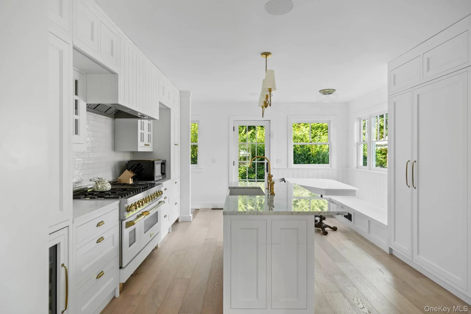 Kitchen featuring white cabinetry, range with two ovens, light wood-style floors, light stone countertops, and a center island with sink Kitchen featuring white cabinetry, range with two ovens, light wood-style floors, light stone countertops, and a center island with sink