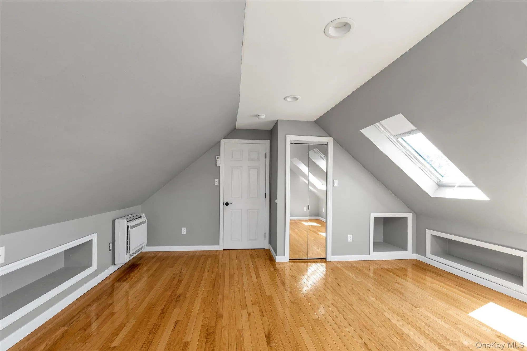 Additional living space with built in features, light wood-style floors, a skylight, lofted ceiling, and a wall unit AC Additional living space with built in features, light wood-style floors, a skylight, lofted ceiling, and a wall unit AC