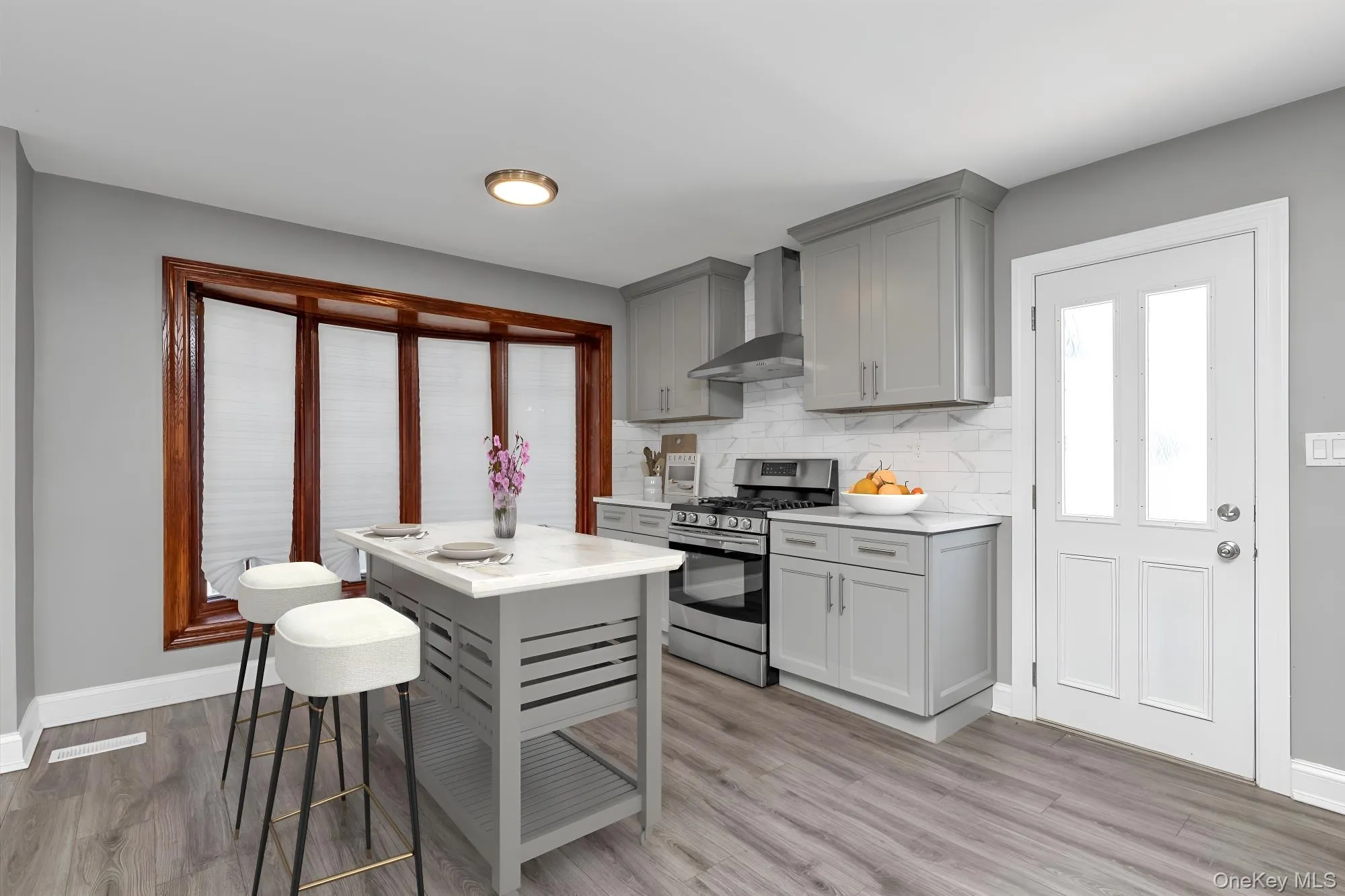 Kitchen with gray cabinets, stainless steel gas stove, decorative backsplash, and wall chimney exhaust hood Kitchen with gray cabinets, stainless steel gas stove, decorative backsplash, and wall chimney exhaust hood