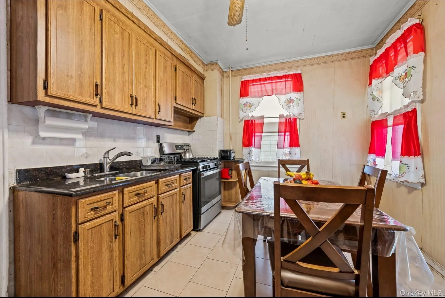 Kitchen featuring stainless steel gas range oven, decorative backsplash, light tile patterned flooring, brown cabinetry, and crown molding Kitchen featuring stainless steel gas range oven, decorative backsplash, light tile patterned flooring, brown cabinetry, and crown molding