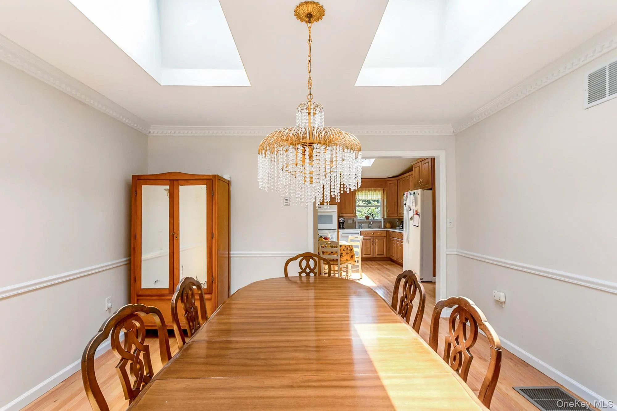 Dining room featuring a skylight, light wood-type flooring, crown molding, and a chandelier Dining room featuring a skylight, light wood-type flooring, crown molding, and a chandelier