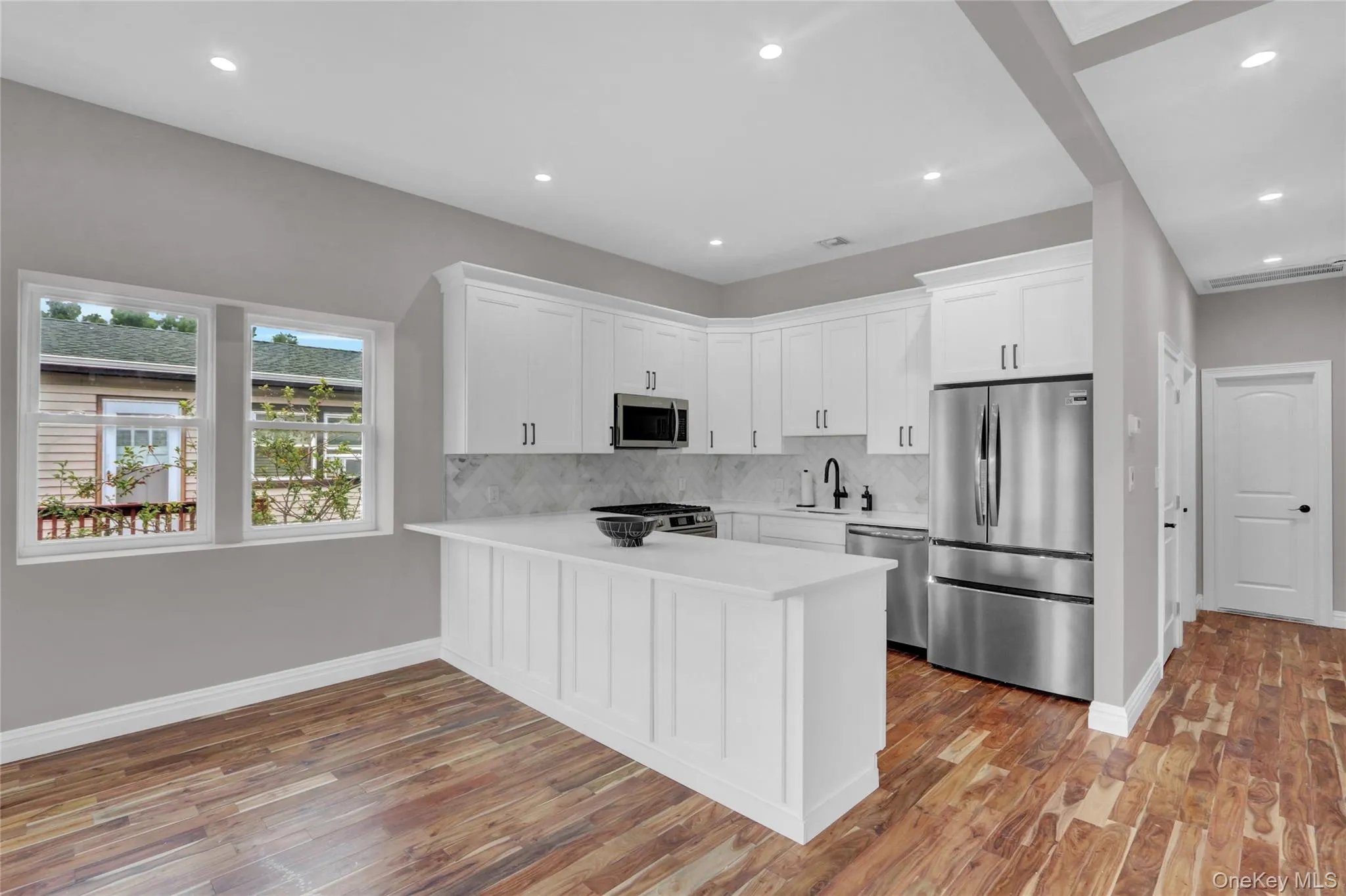 Kitchen with appliances with stainless steel finishes, white cabinets, decorative backsplash, a peninsula, and light wood-style flooring Kitchen with appliances with stainless steel finishes, white cabinets, decorative backsplash, a peninsula, and light wood-style flooring
