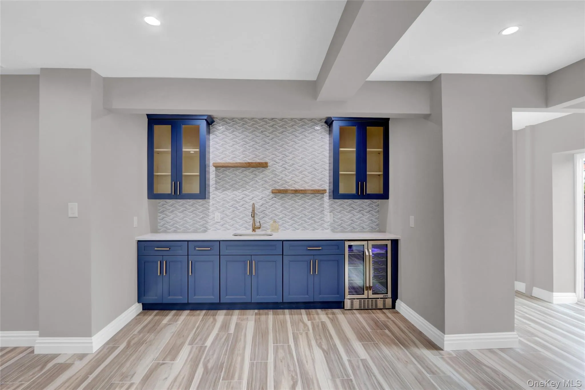Indoor wet bar featuring blue cabinetry, decorative backsplash, glass insert cabinets, wood finish floors, and recessed lighting Indoor wet bar featuring blue cabinetry, decorative backsplash, glass insert cabinets, wood finish floors, and recessed lighting