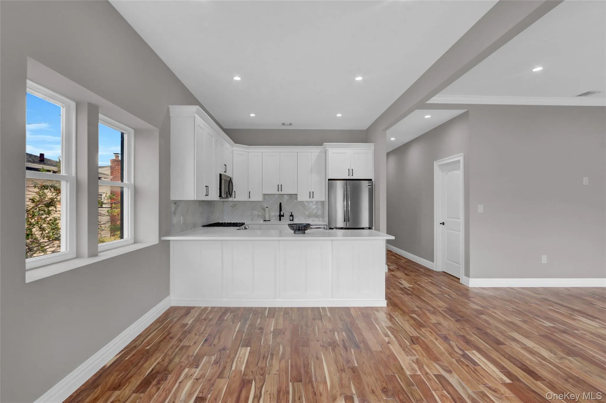 Kitchen featuring white cabinets, light wood-style flooring, a peninsula, backsplash, and open floor plan Kitchen featuring white cabinets, light wood-style flooring, a peninsula, backsplash, and open floor plan