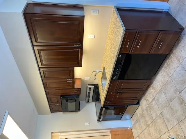 Kitchen featuring black stove, dark brown cabinetry, dishwasher, light stone countertops, and light tile patterned floors Kitchen featuring black stove, dark brown cabinetry, dishwasher, light stone countertops, and light tile patterned floors