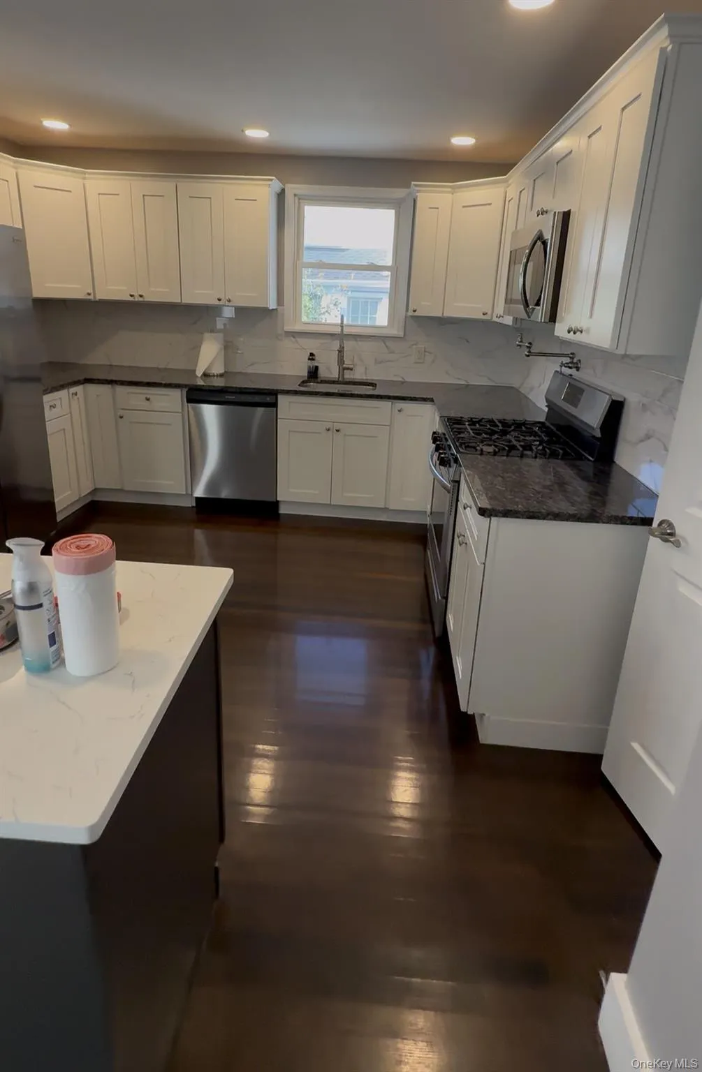 Kitchen with dark stone counters, appliances with stainless steel finishes, white cabinets, decorative backsplash, and dark wood-style flooring Kitchen with dark stone counters, appliances with stainless steel finishes, white cabinets, decorative backsplash, and dark wood-style flooring