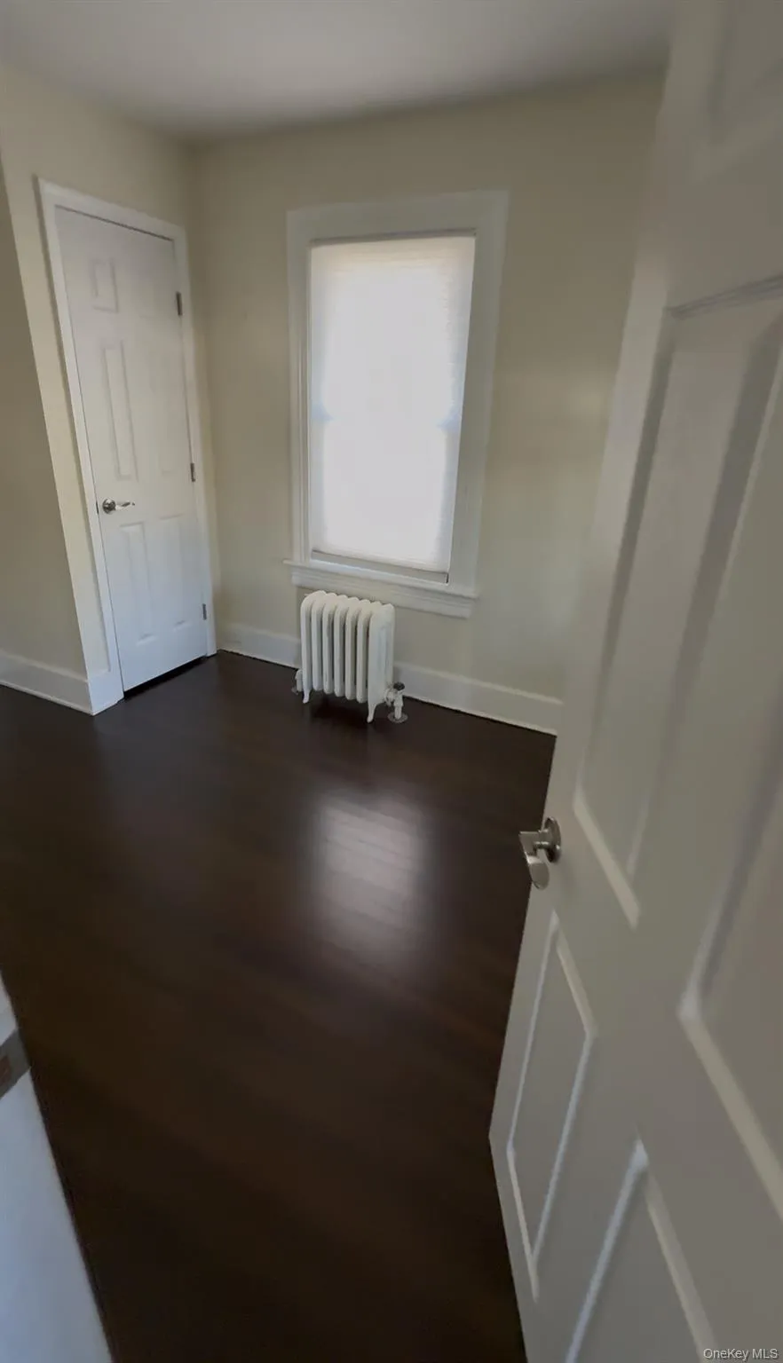 Unfurnished bedroom featuring dark wood-type flooring and radiator Unfurnished bedroom featuring dark wood-type flooring and radiator
