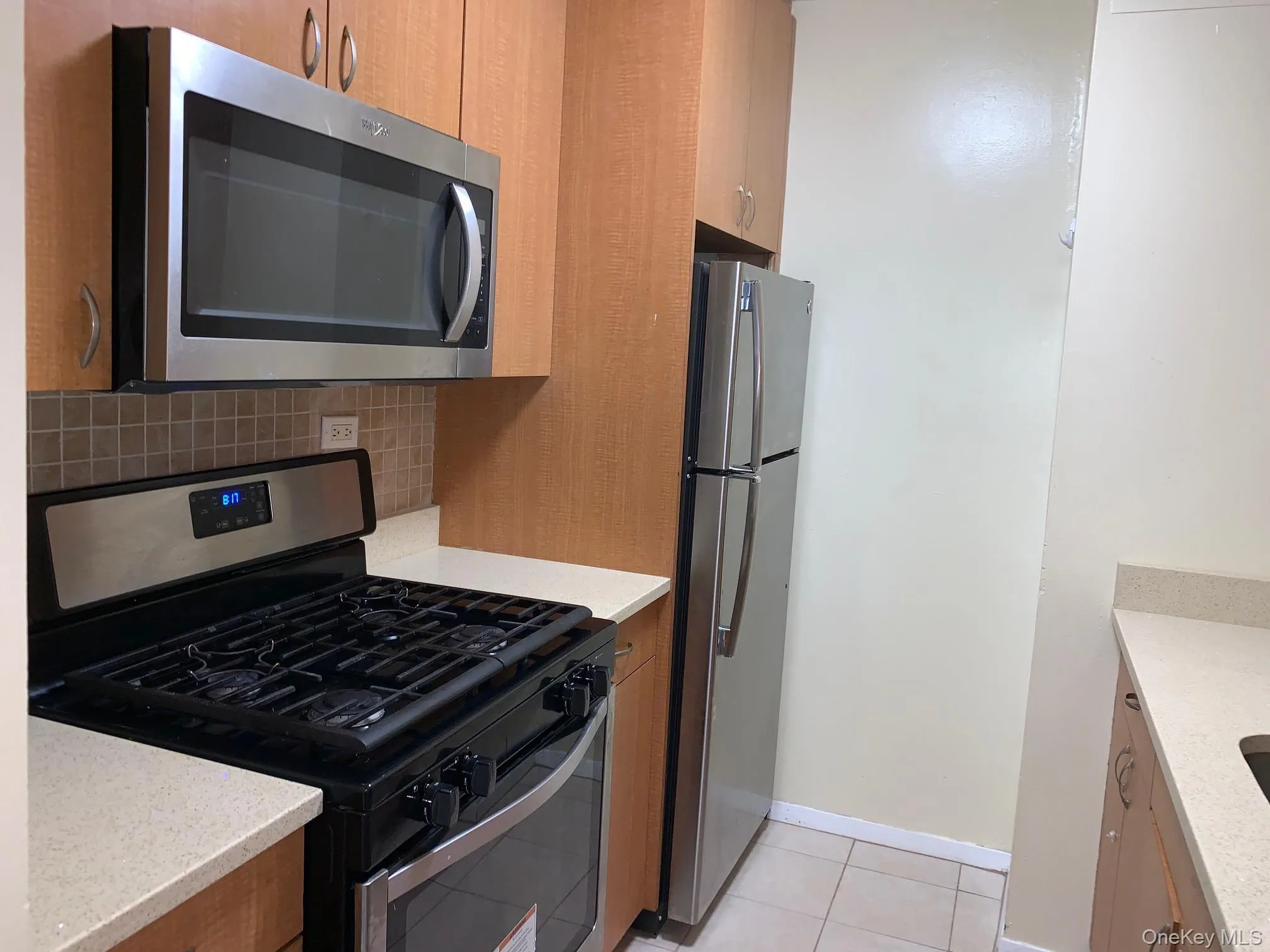 Kitchen with appliances with stainless steel finishes, light stone countertops, light tile patterned flooring, and backsplash Kitchen with appliances with stainless steel finishes, light stone countertops, light tile patterned flooring, and backsplash