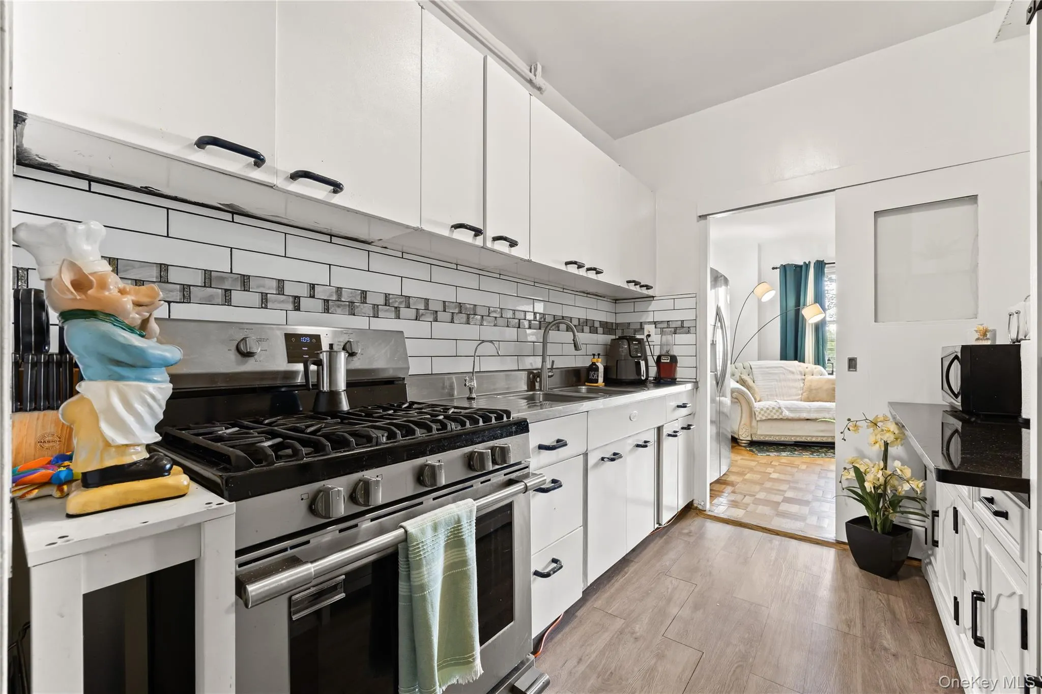 Kitchen with appliances with stainless steel finishes, white cabinetry, decorative backsplash, light wood-type flooring, and dark countertops Kitchen with appliances with stainless steel finishes, white cabinetry, decorative backsplash, light wood-type flooring, and dark countertops