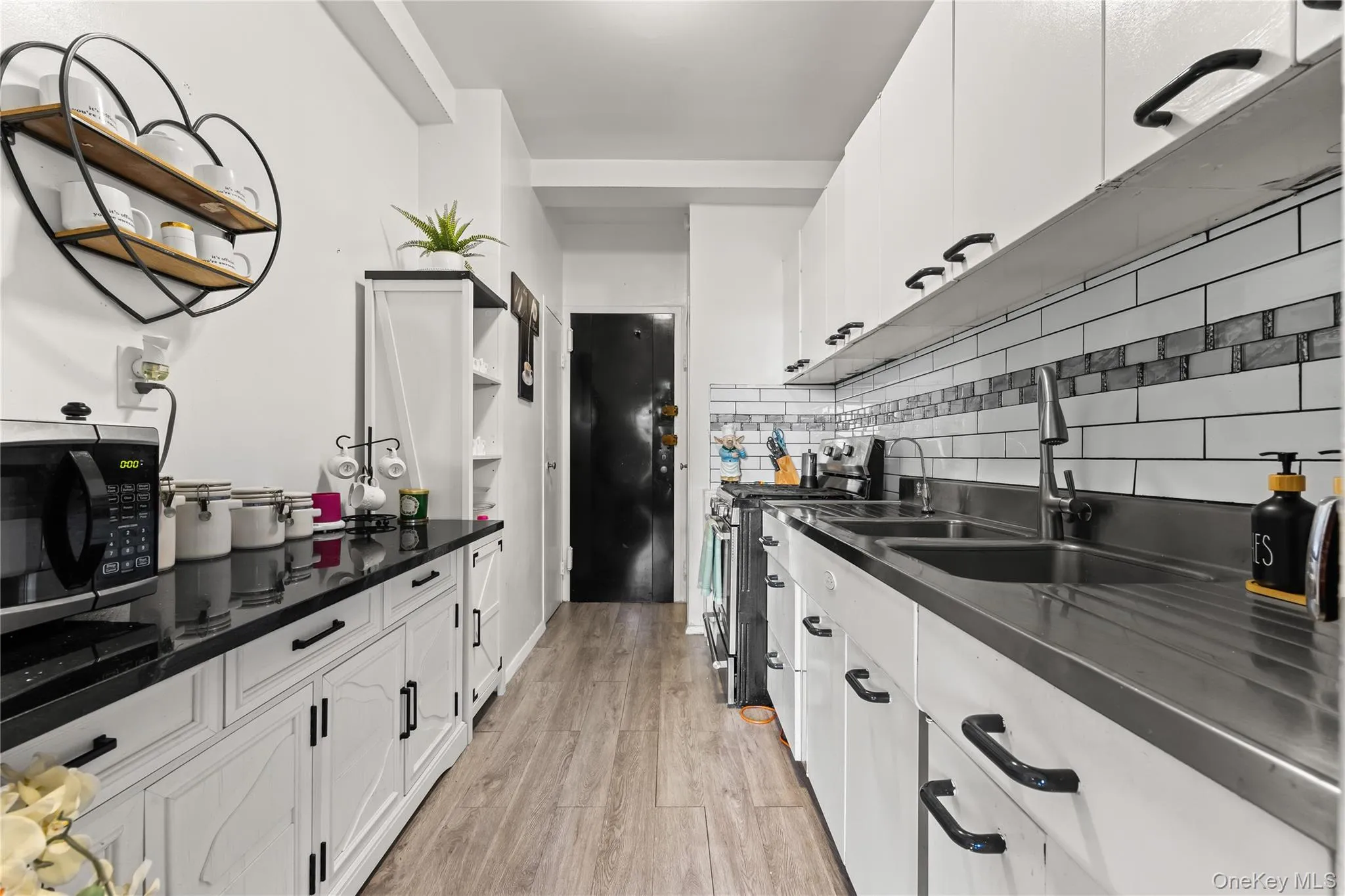 Kitchen featuring white cabinets, open shelves, appliances with stainless steel finishes, light wood-type flooring, and backsplash Kitchen featuring white cabinets, open shelves, appliances with stainless steel finishes, light wood-type flooring, and backsplash