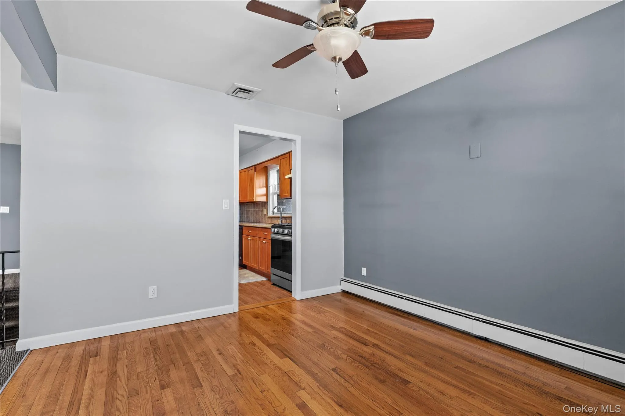 Empty room with baseboard heating, light wood finished floors, and ceiling fan Empty room with baseboard heating, light wood finished floors, and ceiling fan
