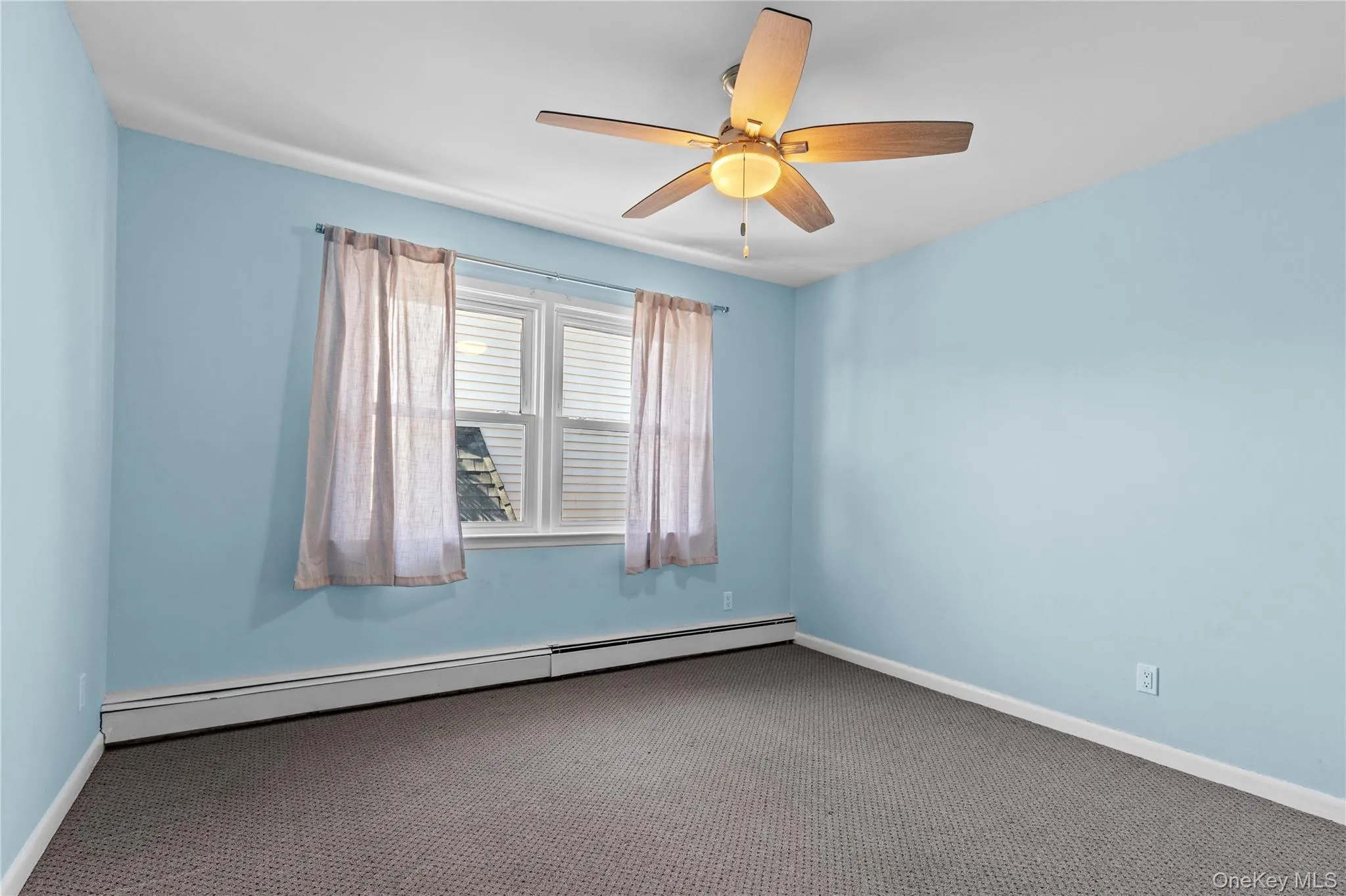 Empty room with baseboard heating, carpet flooring, and a ceiling fan Empty room with baseboard heating, carpet flooring, and a ceiling fan