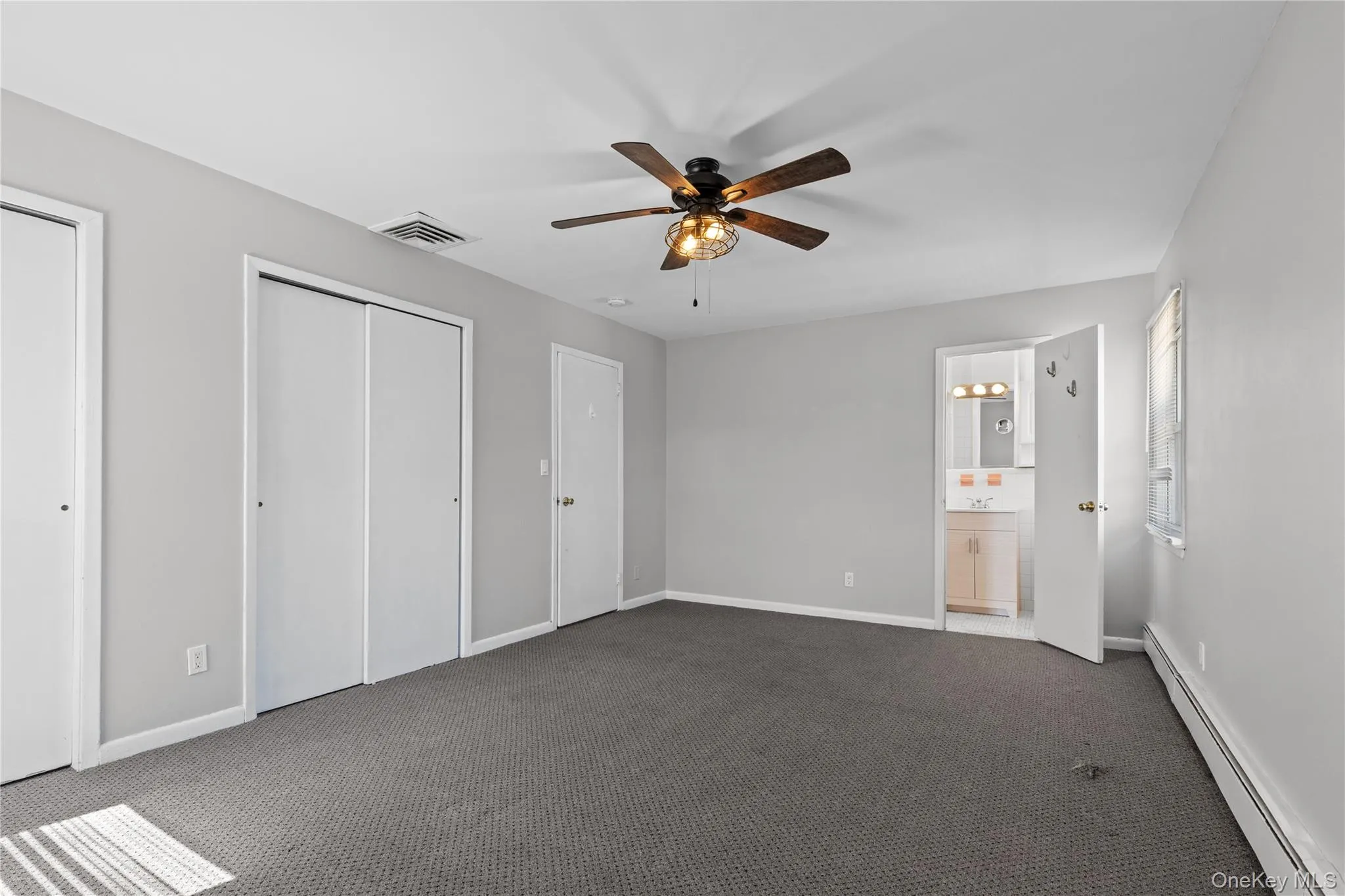 Unfurnished bedroom featuring a baseboard radiator, carpet flooring, a ceiling fan, and two closets Unfurnished bedroom featuring a baseboard radiator, carpet flooring, a ceiling fan, and two closets