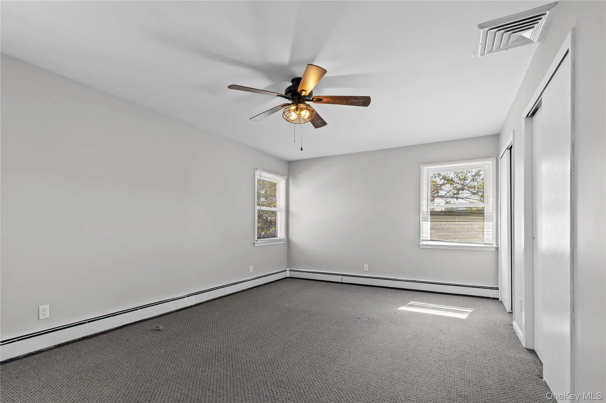 Unfurnished bedroom featuring carpet floors, a baseboard heating unit, and multiple windows Unfurnished bedroom featuring carpet floors, a baseboard heating unit, and multiple windows