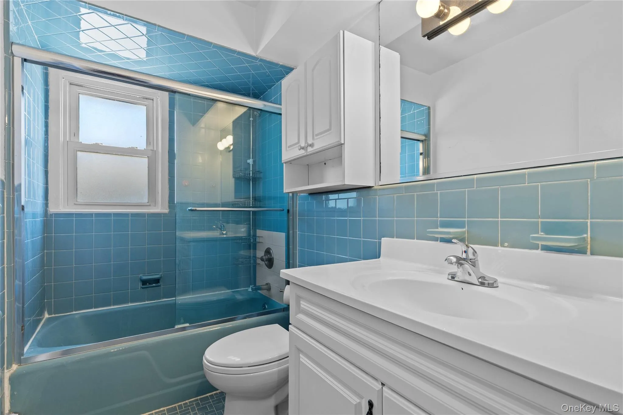 Full bathroom featuring bath / shower combo with glass door, vanity, tile walls, and tile patterned flooring Full bathroom featuring bath / shower combo with glass door, vanity, tile walls, and tile patterned flooring