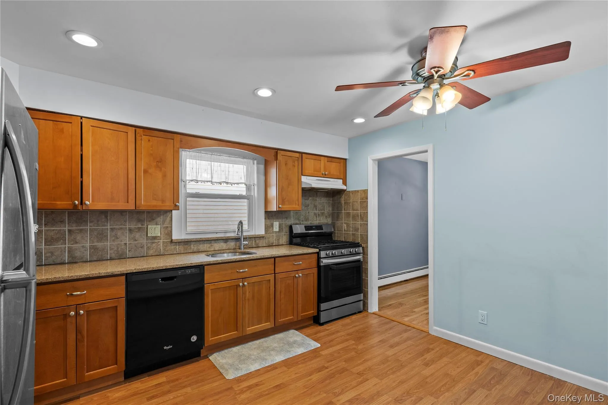 Kitchen with brown cabinets, decorative backsplash, stainless steel appliances, light stone counters, and recessed lighting Kitchen with brown cabinets, decorative backsplash, stainless steel appliances, light stone counters, and recessed lighting