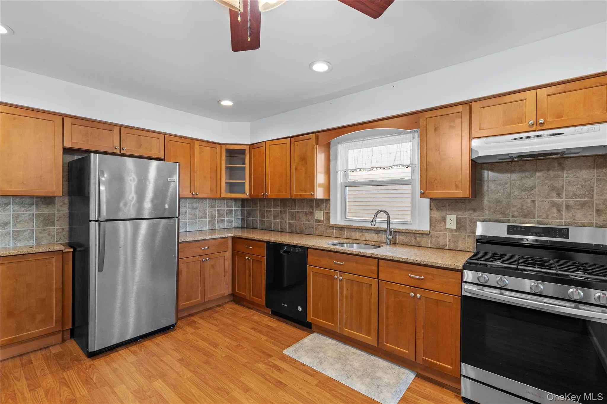 Kitchen with appliances with stainless steel finishes, brown cabinets, light stone counters, and recessed lighting Kitchen with appliances with stainless steel finishes, brown cabinets, light stone counters, and recessed lighting
