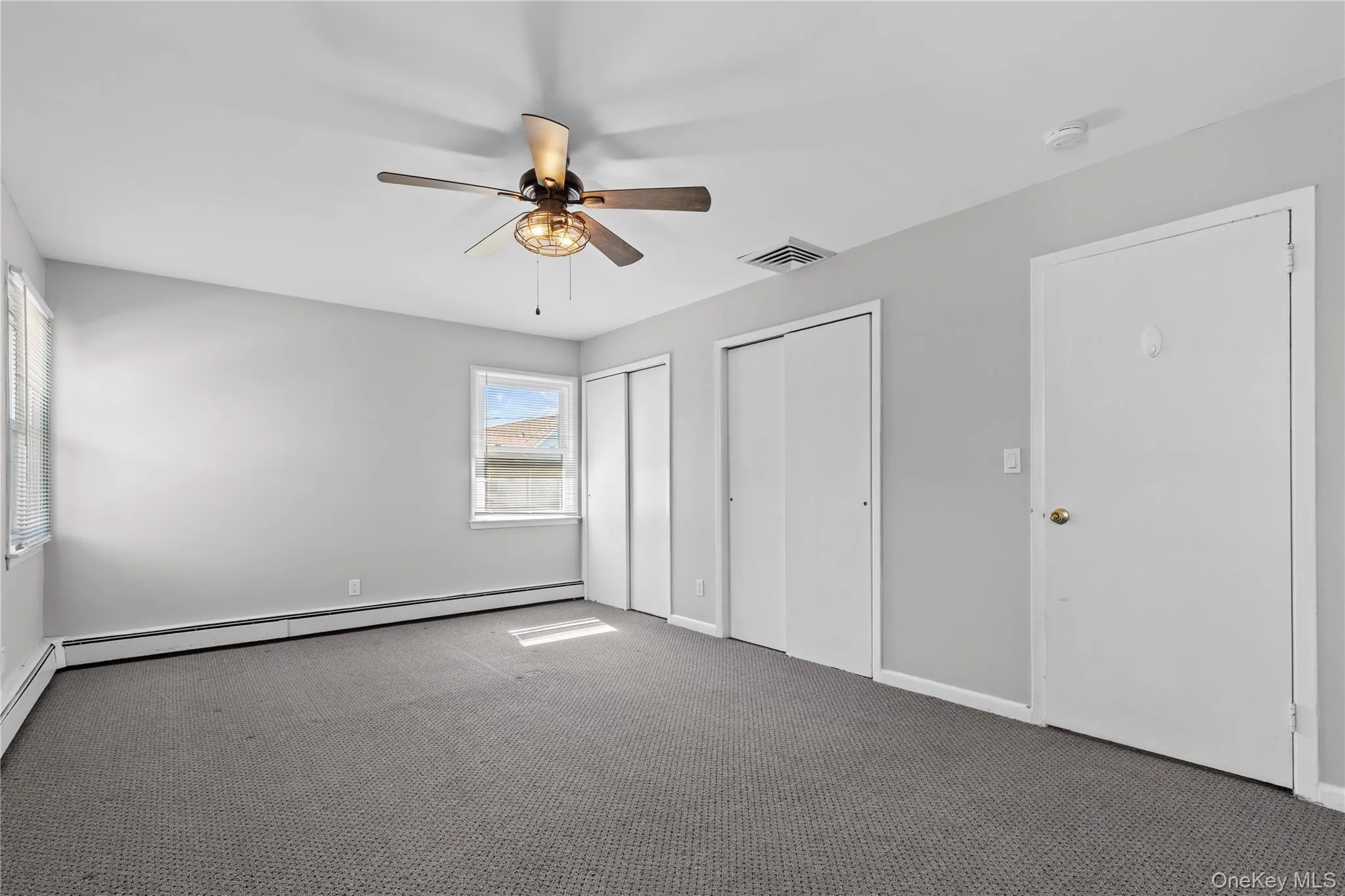 Unfurnished bedroom featuring two closets, carpet flooring, a ceiling fan, and a baseboard heating unit Unfurnished bedroom featuring two closets, carpet flooring, a ceiling fan, and a baseboard heating unit