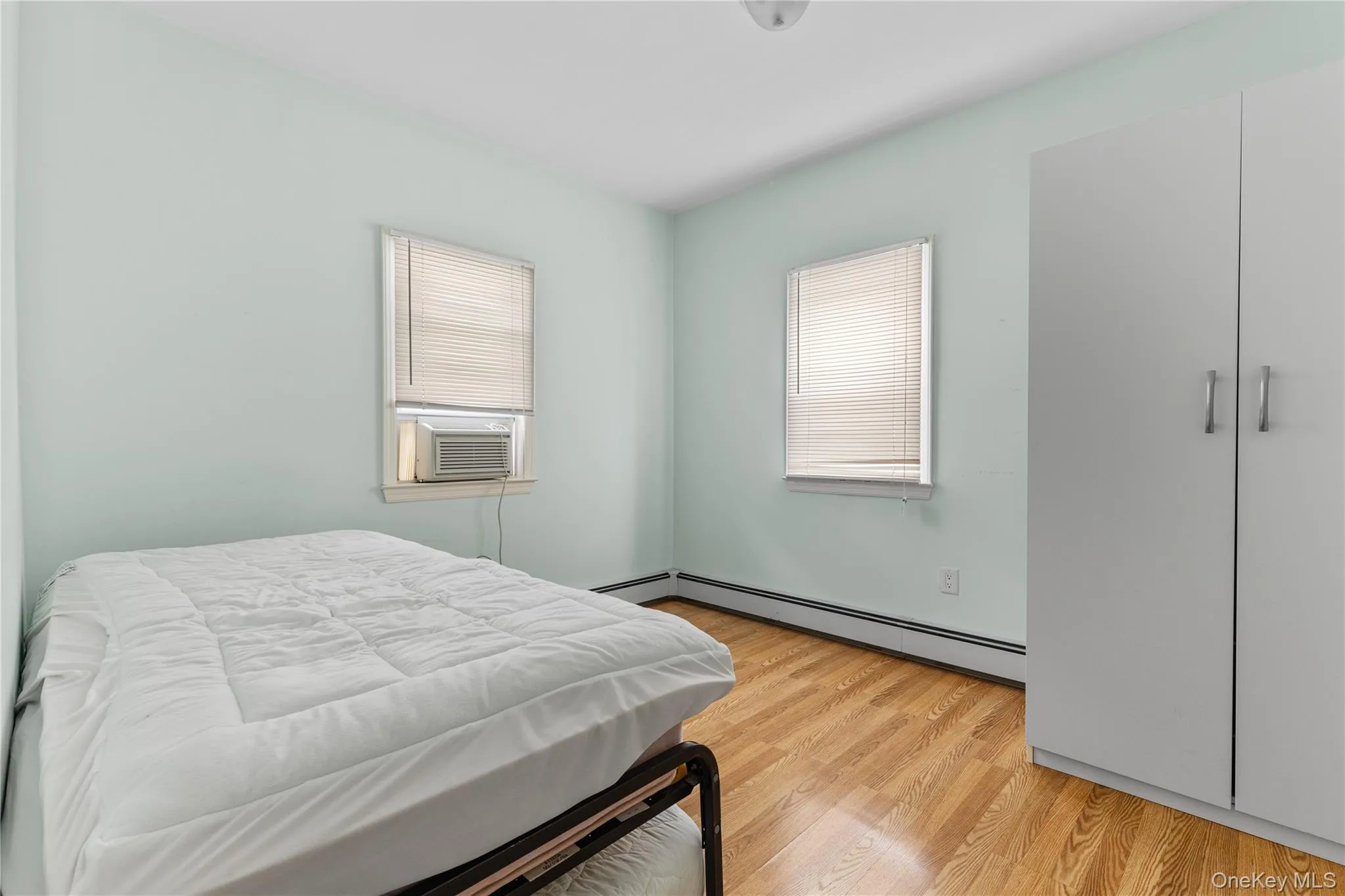 Bedroom featuring light wood finished floors, cooling unit, and a baseboard heating unit Bedroom featuring light wood finished floors, cooling unit, and a baseboard heating unit