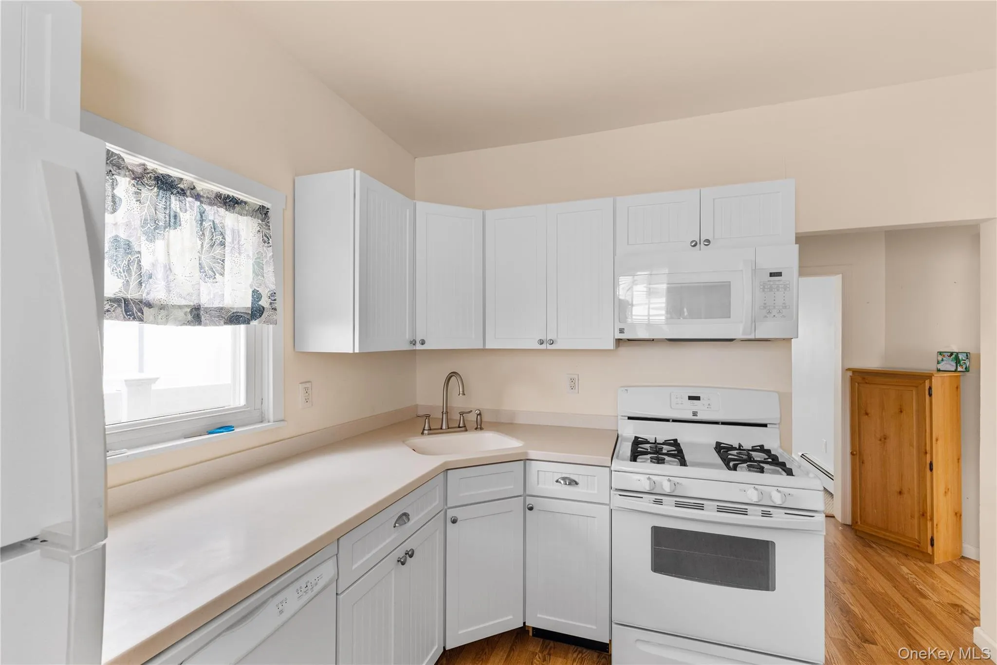 Kitchen with white appliances, light countertops, light wood finished floors, white cabinets, and a baseboard radiator Kitchen with white appliances, light countertops, light wood finished floors, white cabinets, and a baseboard radiator