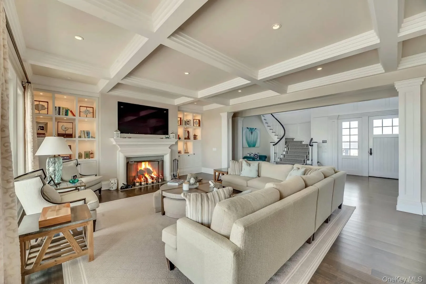 Living area with wood finished floors, beamed ceiling, a glass covered fireplace, stairs, and coffered ceiling Living area with wood finished floors, beamed ceiling, a glass covered fireplace, stairs, and coffered ceiling
