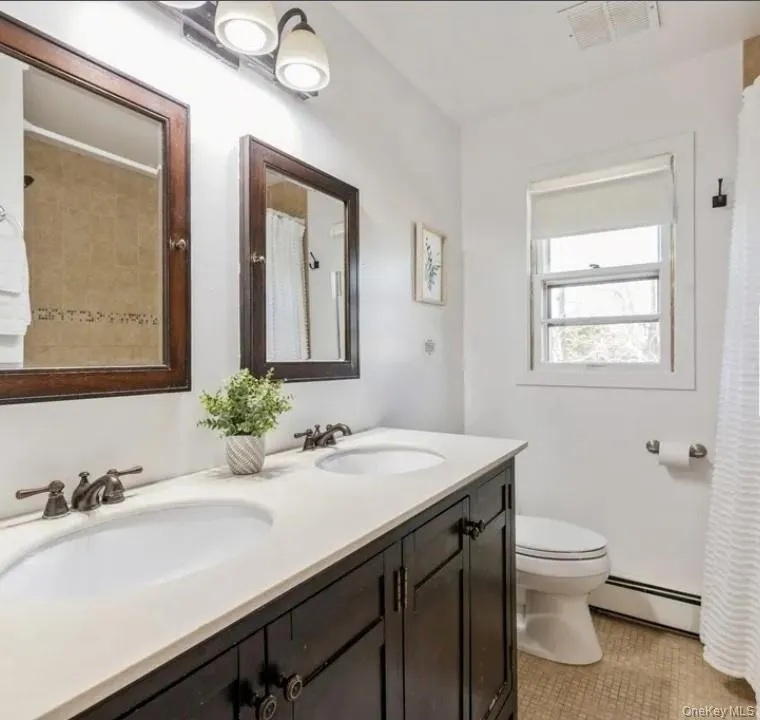 Bathroom with double vanity, a baseboard radiator, light tile patterned floors, and curtained shower Bathroom with double vanity, a baseboard radiator, light tile patterned floors, and curtained shower
