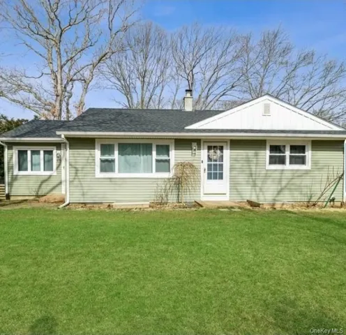 Ranch-style house featuring a front yard, a chimney, a shingled roof, and board and batten siding