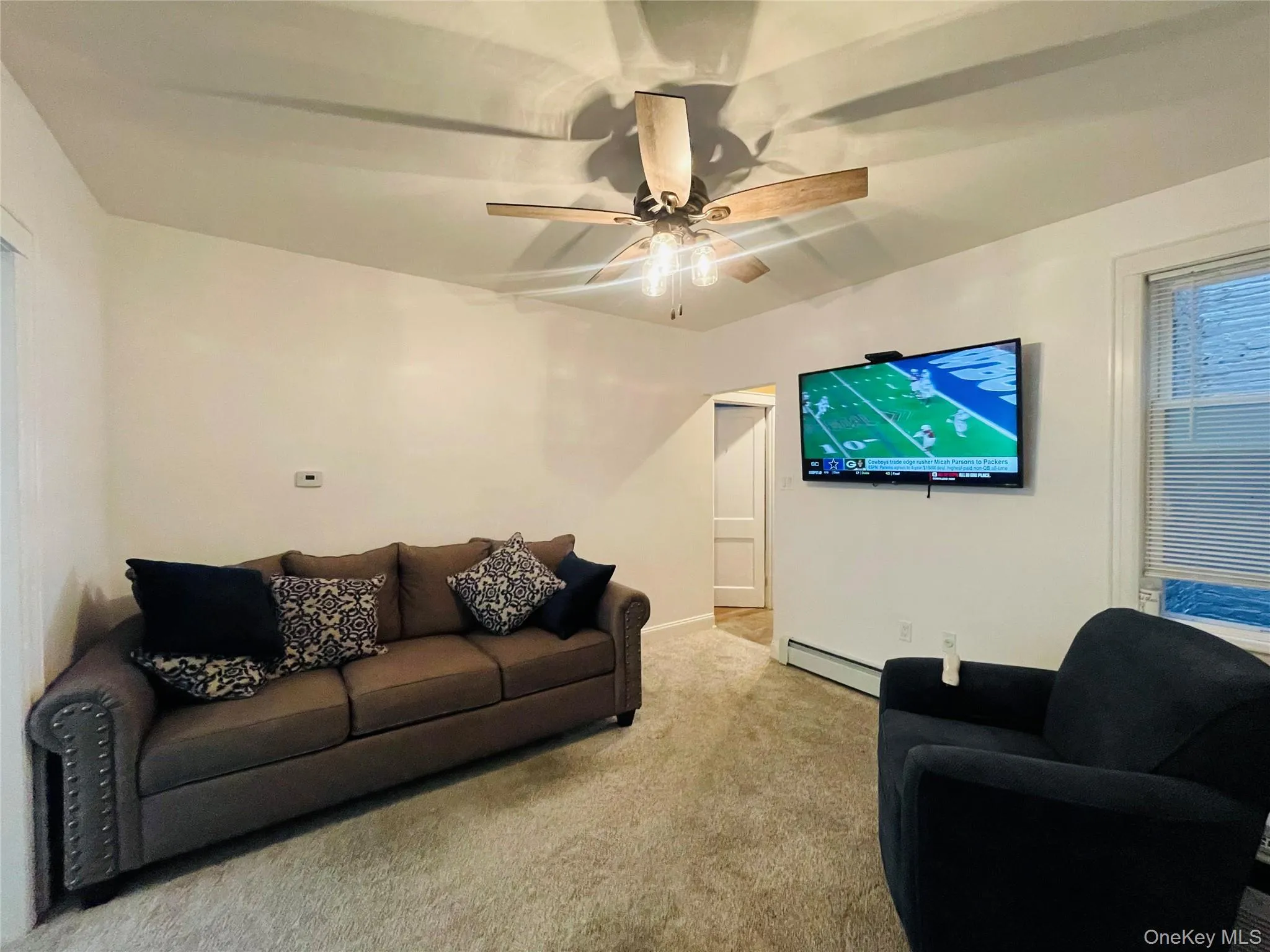 Carpeted living area featuring baseboard heating and a ceiling fan Carpeted living area featuring baseboard heating and a ceiling fan