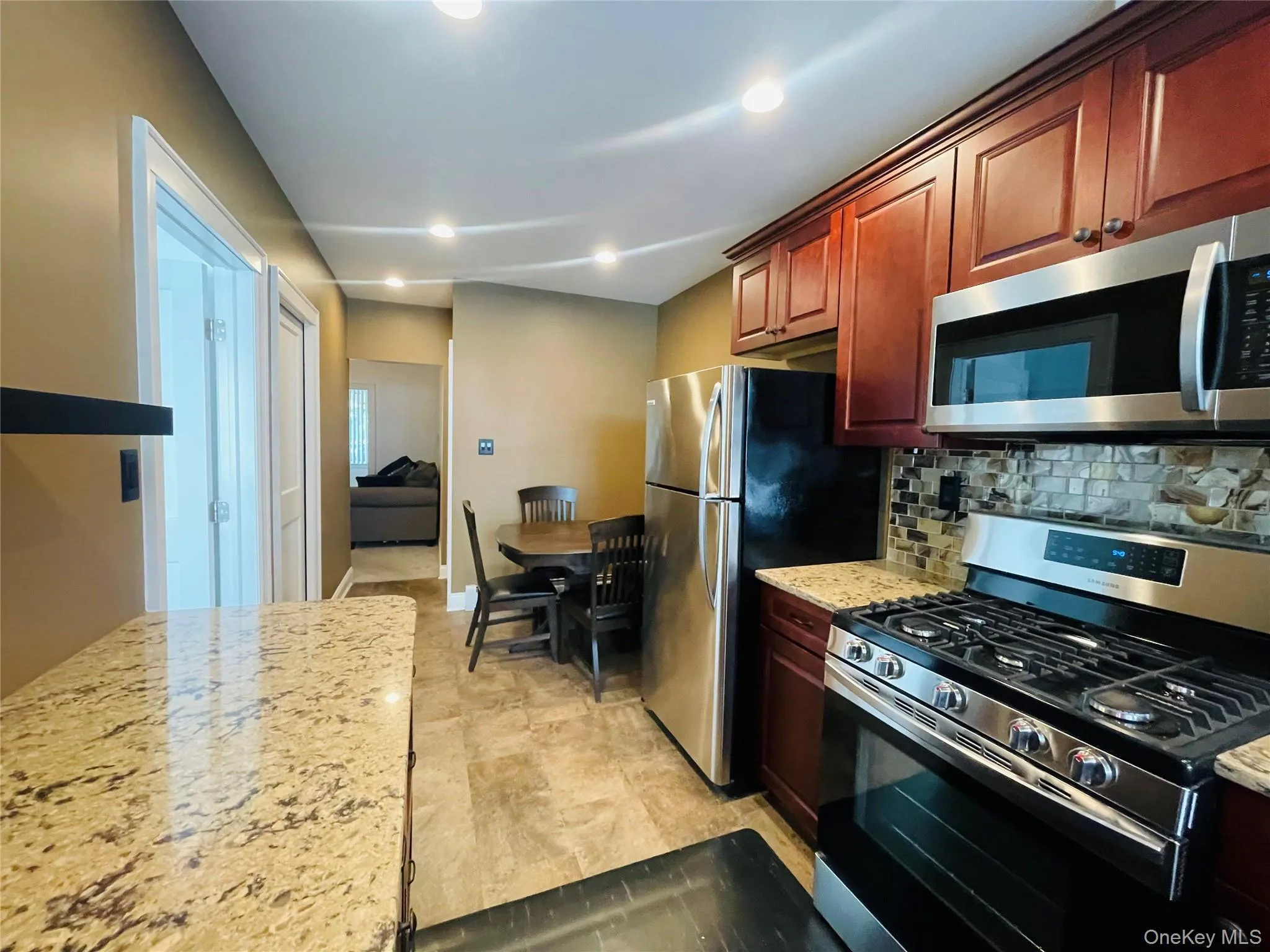 Kitchen featuring appliances with stainless steel finishes, light stone counters, decorative backsplash, recessed lighting, and light tile patterned floors Kitchen featuring appliances with stainless steel finishes, light stone counters, decorative backsplash, recessed lighting, and light tile patterned floors