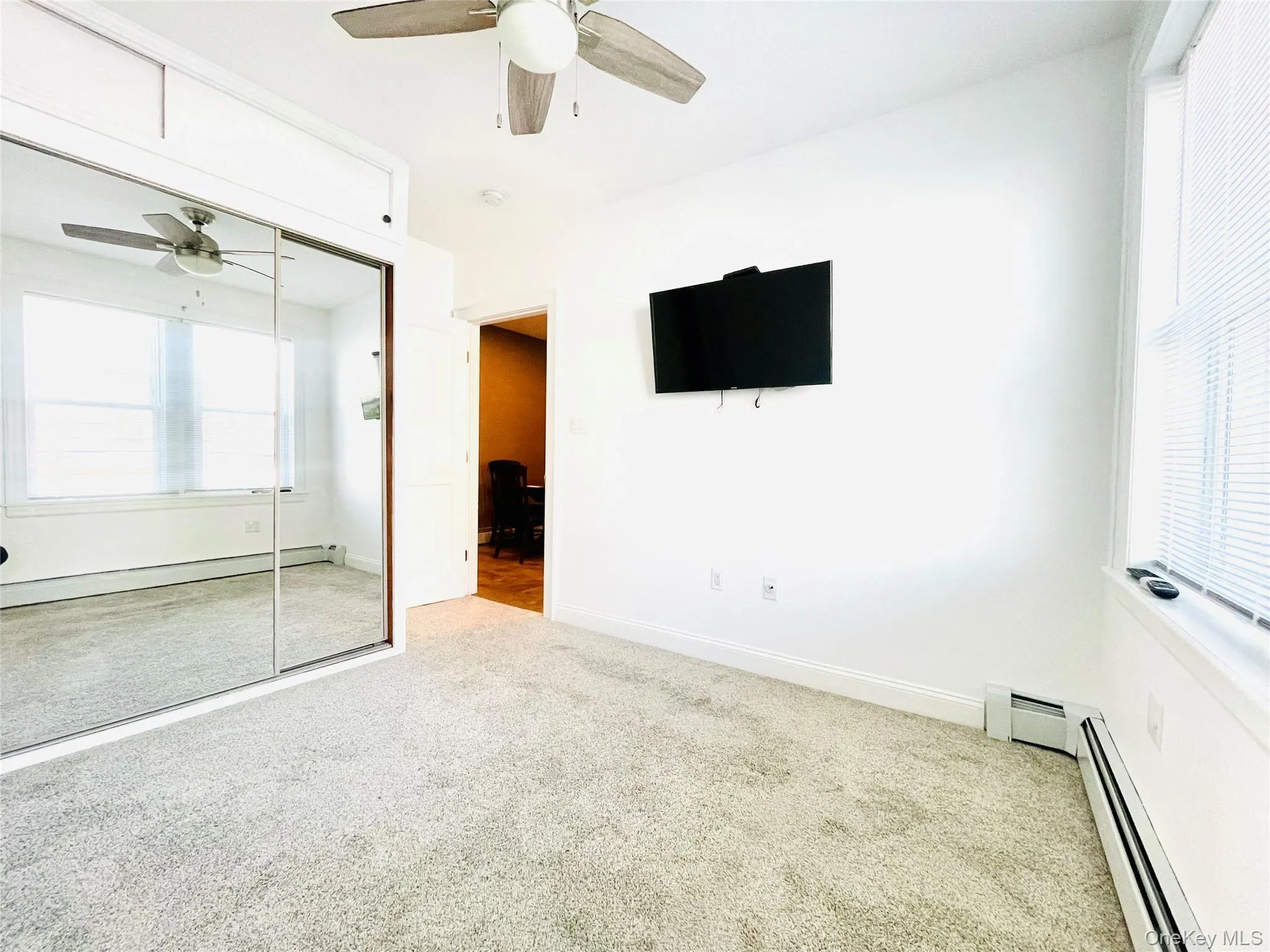 Unfurnished bedroom with carpet flooring, ceiling fan, a closet, and a baseboard radiator Unfurnished bedroom with carpet flooring, ceiling fan, a closet, and a baseboard radiator
