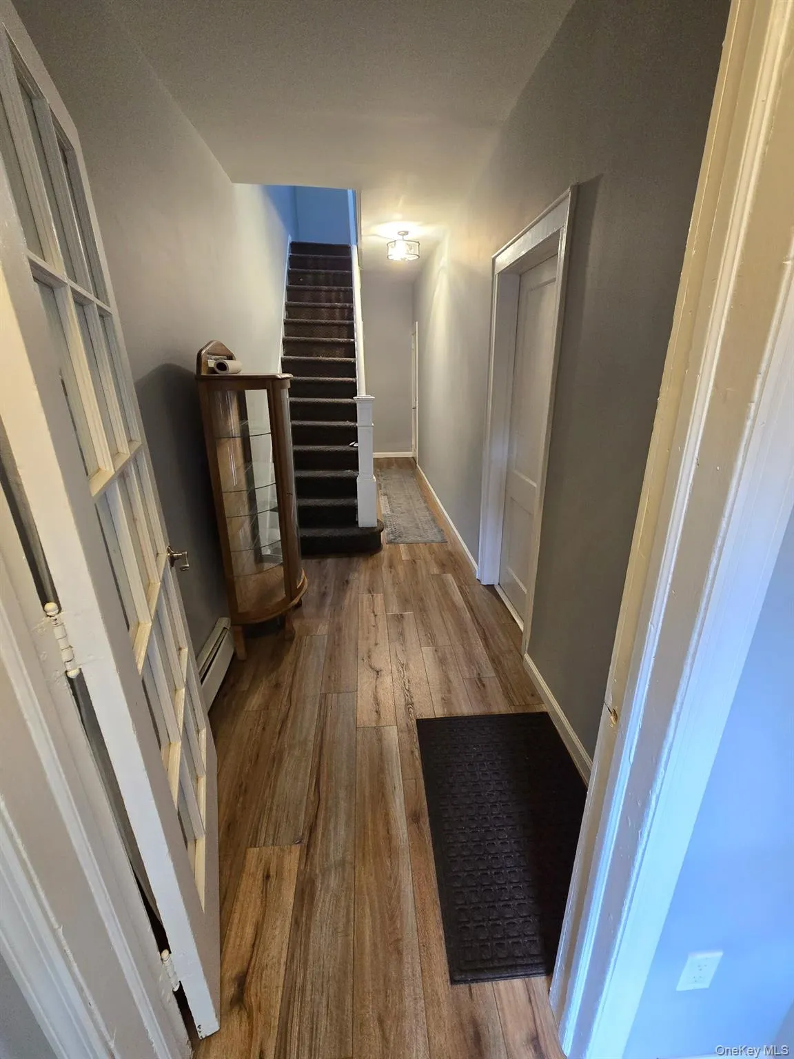 Corridor featuring hardwood / wood-style flooring, stairway, and a baseboard heating unit Corridor featuring hardwood / wood-style flooring, stairway, and a baseboard heating unit
