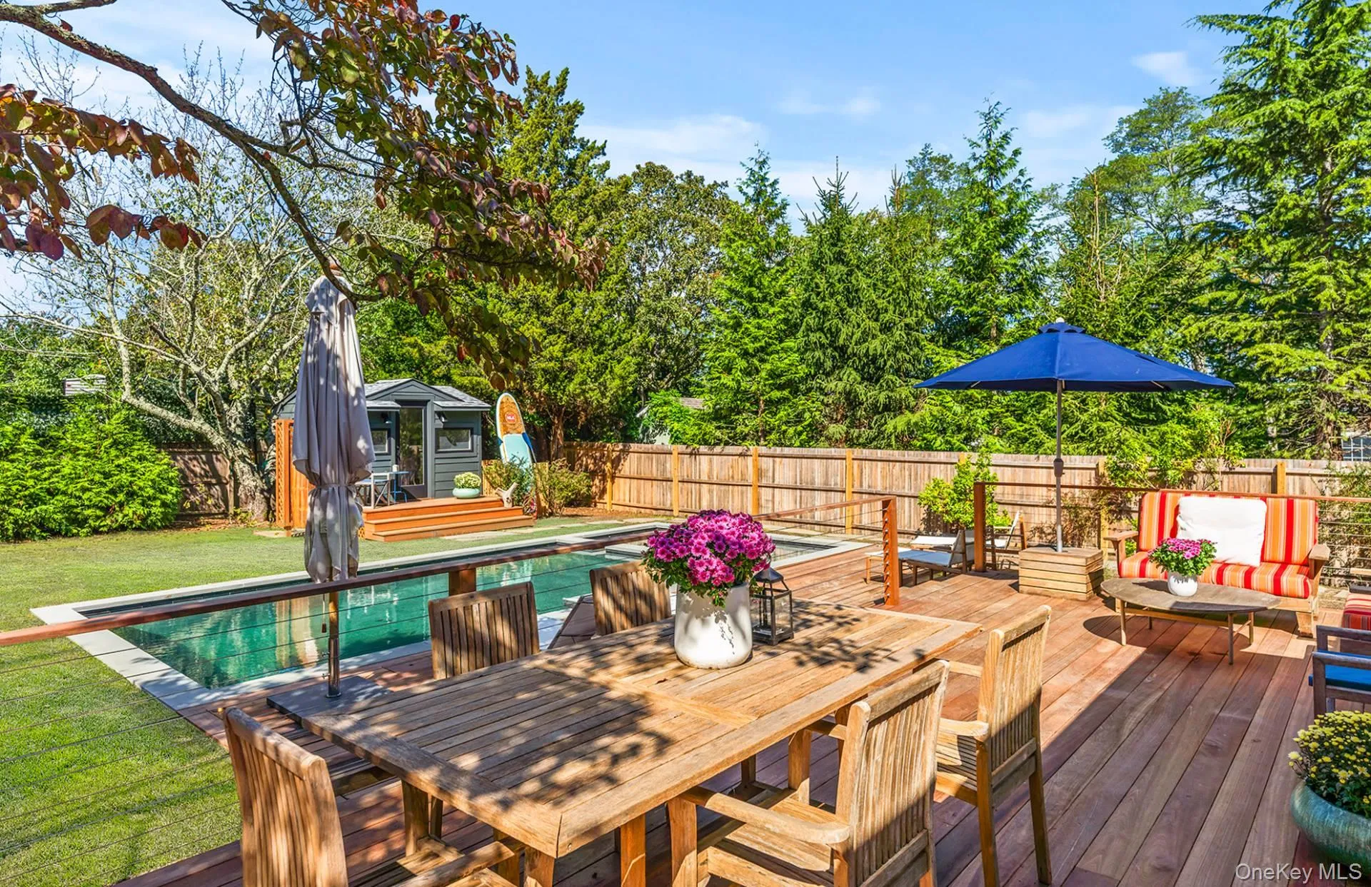 Wooden deck with outdoor dining area, a fenced backyard, view of wooded area, an outdoor structure, and a patio area Wooden deck with outdoor dining area, a fenced backyard, view of wooded area, an outdoor structure, and a patio area