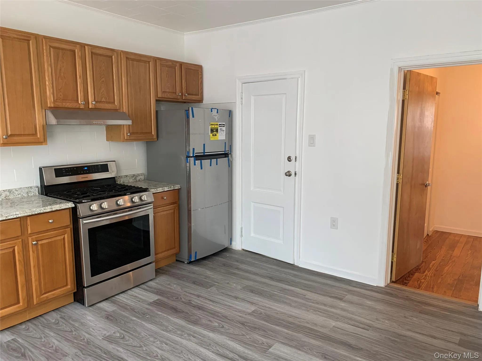 Kitchen with brown cabinetry, appliances with stainless steel finishes, light wood-type flooring, and light stone counters Kitchen with brown cabinetry, appliances with stainless steel finishes, light wood-type flooring, and light stone counters